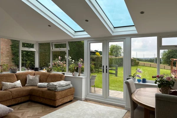 Bright conservatory with roof windows, glazed doors, corner sofa, dining table and garden views in Chichester, West Sussex